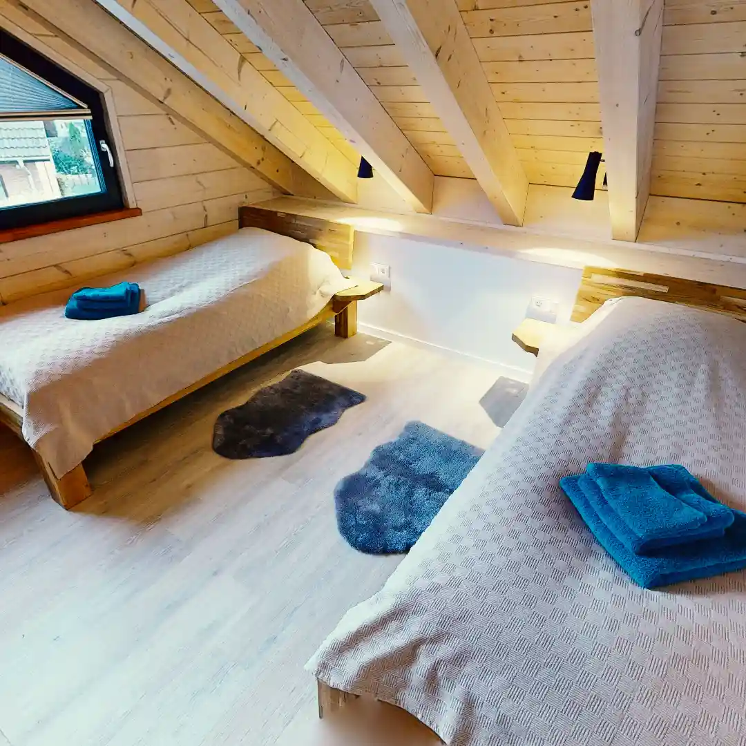 Ein gemütliches Schlafzimmer mit zwei Einzelbetten, Holzrahmen und blauen Handtüchern auf den Betten, Holzdecke und zwei Teppichen auf dem Boden. Ideal für Immobilienfotografie.