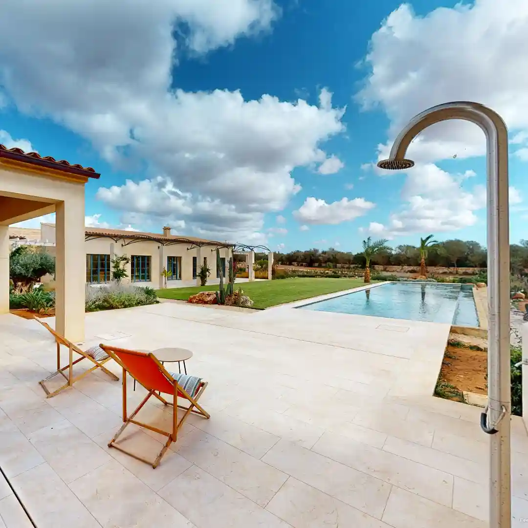 Ein Standbild aus einer virtuellen Tour von raum media, entstanden für die Penta Gruppe. Zu sehen ist eine Finca in Mallorca mit einem eleganten Pool, umgeben von einer grünen Rasenfläche und Palmen. Im Vordergrund stehen zwei Liegestühle und ein kleiner Tisch auf der Terrasse. Der Himmel ist teilweise bewölkt, was eine entspannte Atmosphäre schafft.