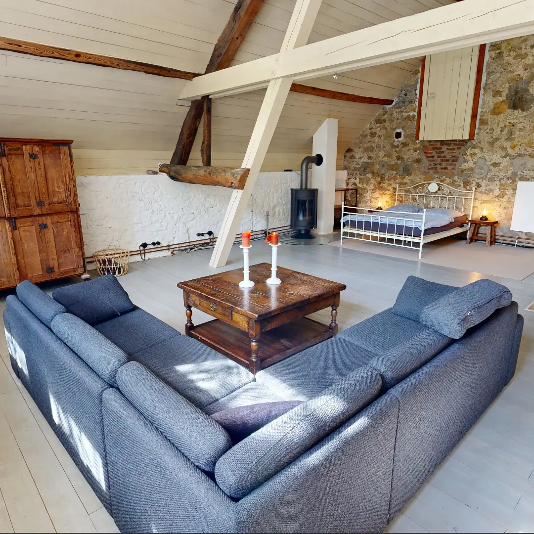 Gemütlicher Wohnbereich in einer Ferienunterkunft mit einem grauen Sofa, einem Holztisch mit Kerzen und einem Bett im Hintergrund.