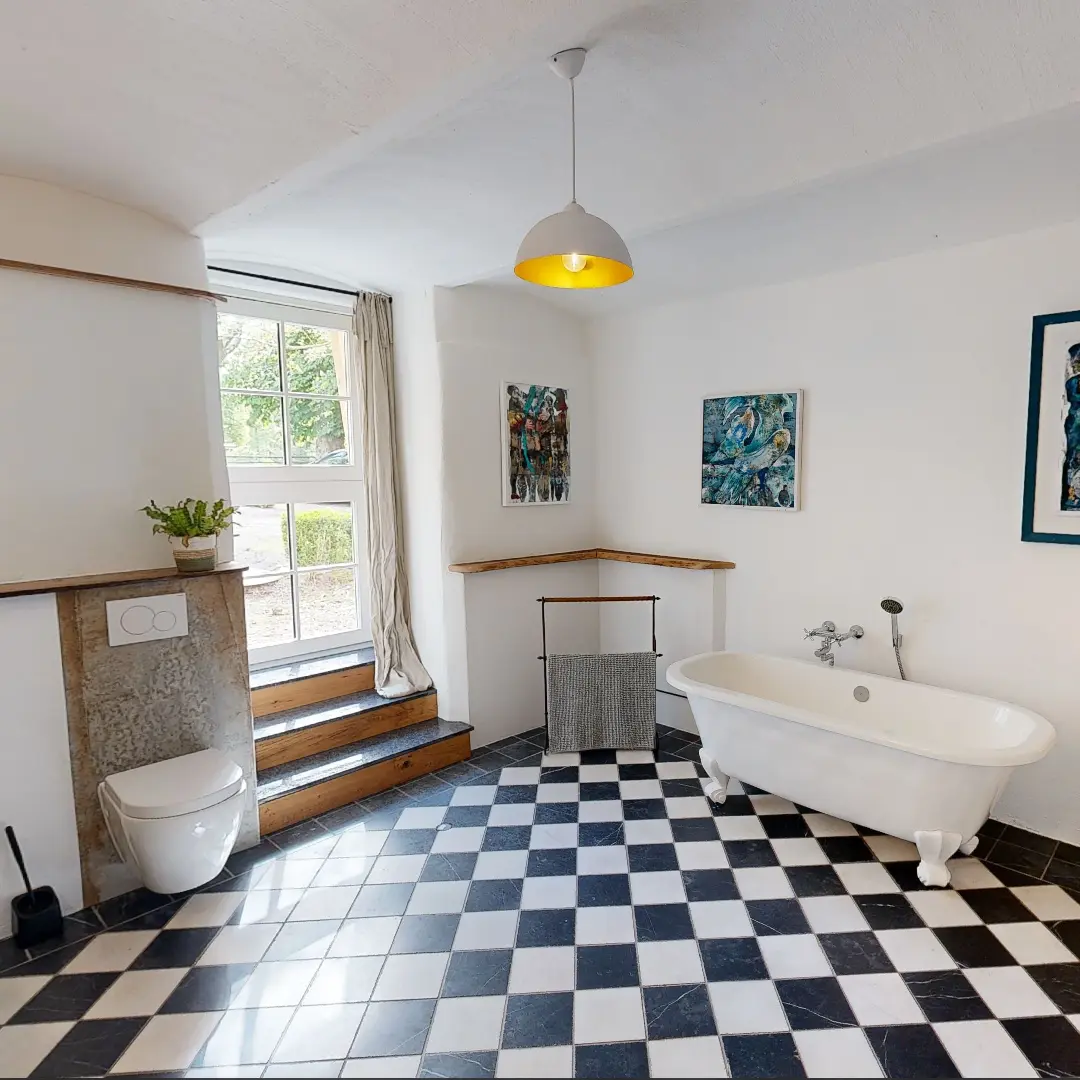 Badezimmer mit freistehender Badewanne, modernen Fliesen in Schwarz-Weiß, Fenster mit Vorhängen und Kunstwerken an der Wand.