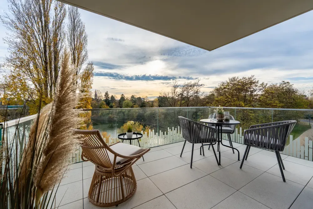 Balkon mit zwei Stühlen und einem Tisch, umgeben von Pflanzen, mit Blick auf den Albertussee in Düsseldorf. Beispiel für Immobilienfotografie von raum media.