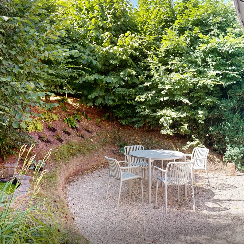 Gartenbereich mit einem runden Tisch und vier Stühlen, umgeben von üppigem Grün.