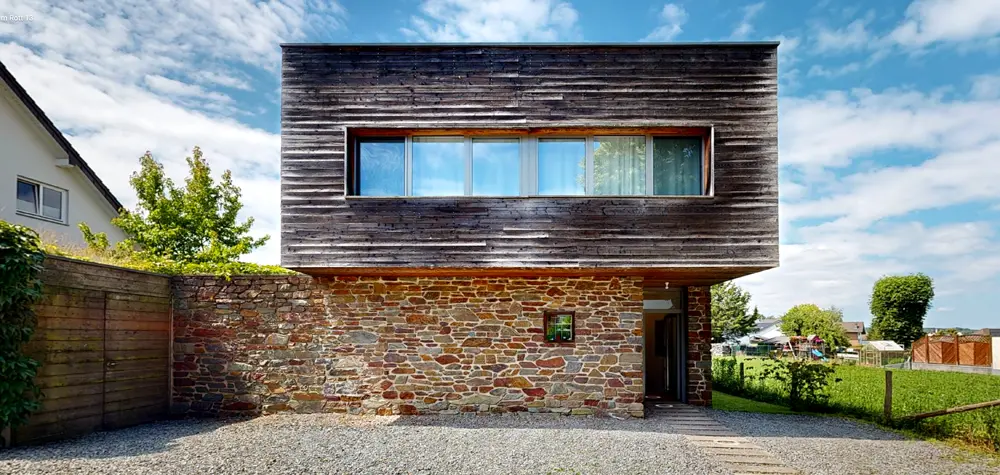 Moderne Immobilie mit Holz- und Steinfassade, umgeben von Bäumen und einem grünen Garten.