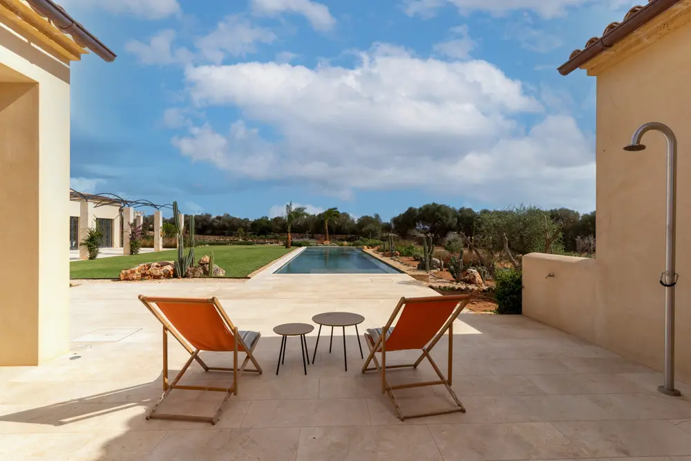 Terrasse mit zwei orangefarbenen Liegestühlen und einem kleinen Tisch, Blick auf einen Pool und einen gepflegten Garten.