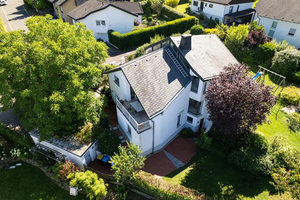 Luftaufnahme eines modernen Hauses mit Garten, umgeben von Bäumen und Nachbarhäusern.