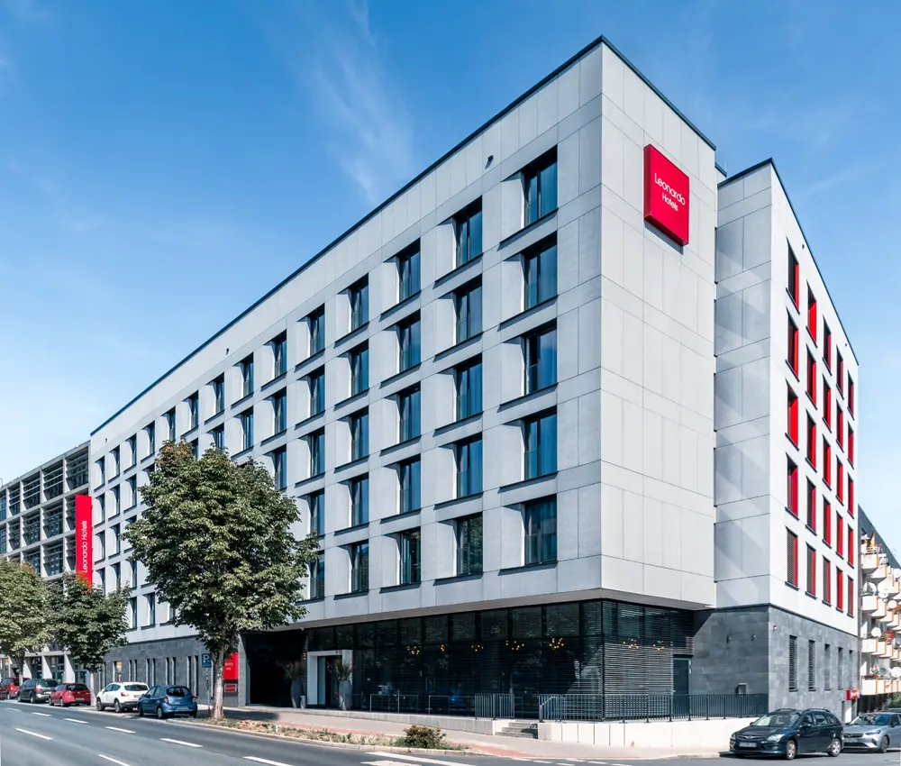 Moderner Hotelbau mit grauer Fassade und großen Fenstern, gekennzeichnet durch das rote Logo von Leonardo Hotel.