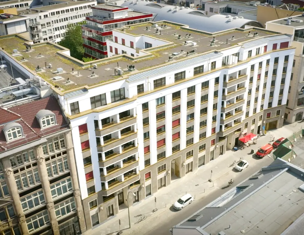 Moderne Wohngebäude mit mehreren Etagen und Balkonen, angrenzend an ältere Architektur, in einer urbanen Umgebung.
