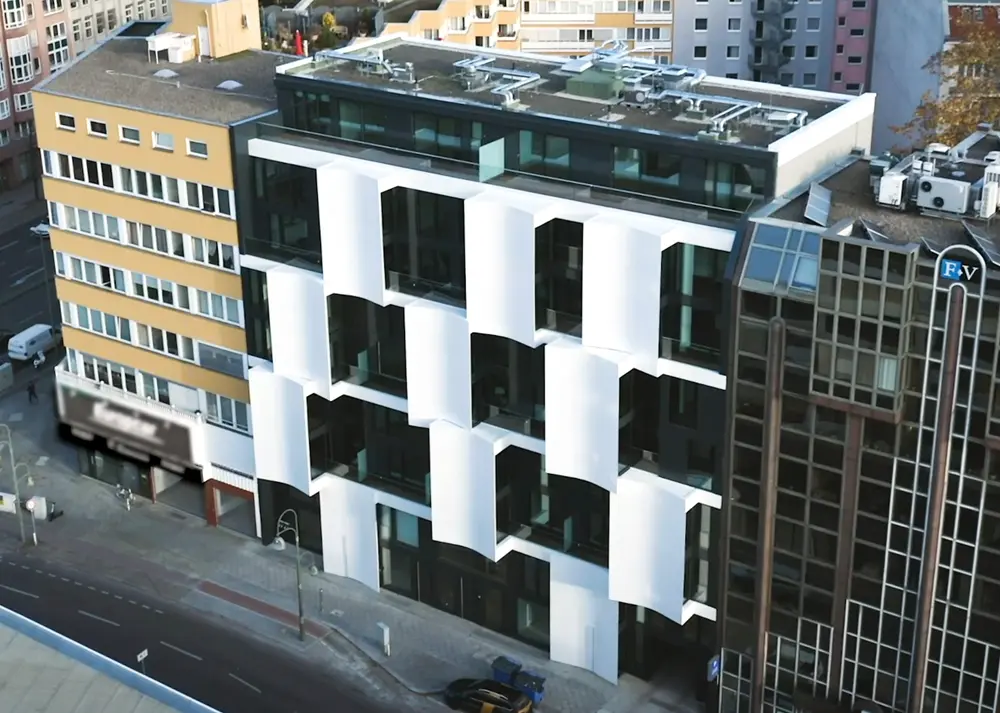 Modernes Gebäude mit einer Fassade aus weißen und schwarzen Elementen. Die Struktur zeigt eine kreative Anordnung von Balkonen und Fenstern, die eine einzigartige architektonische Gestaltung bieten. Im Hintergrund sind weitere Gebäude zu sehen.
