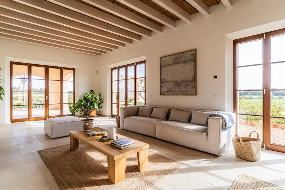 Heller Wohnraum mit einem modernen Sofa, einem Holztisch, Pflanzen und großen Fenstern, die auf eine Gartenlandschaft blicken, ideal für Immobilienfotografie.