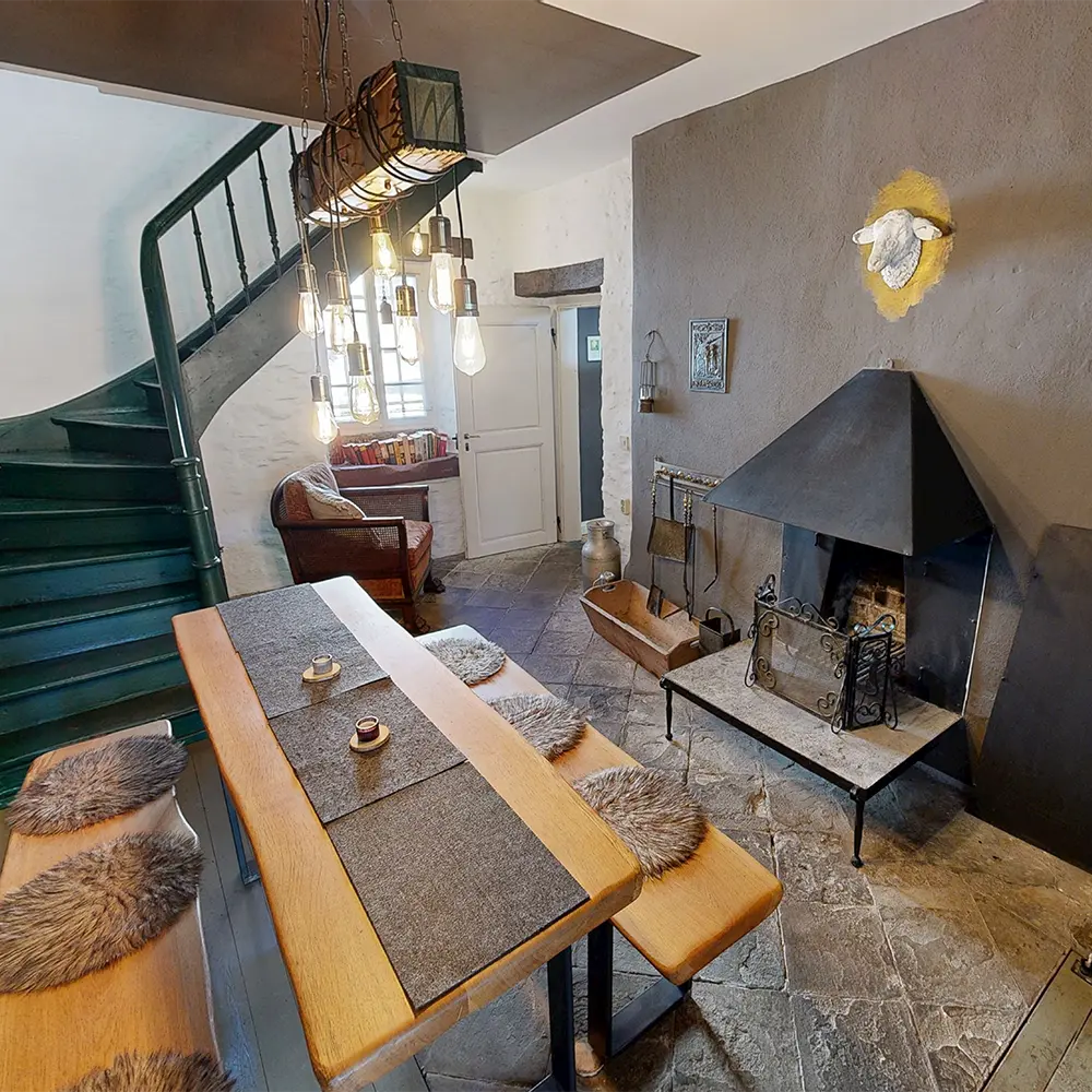 Ein moderner Essbereich mit einem Holztisch, weißen Stühlen, zwei Kerzenhaltern und einem Glasbehälter. An der Wand hängt ein Kunstwerk, das eine lichtdurchflutete Treppe zeigt.